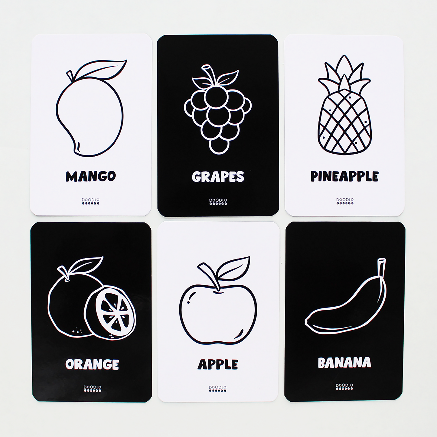 Six flash cards with fruit illustrations; three white background, three black, labeled Mango, Grapes, Pineapple, Orange, Apple, Banana